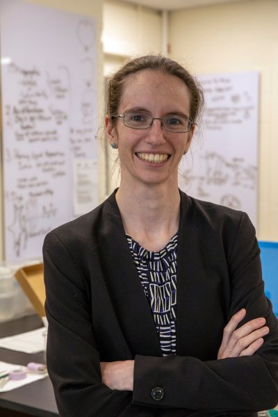 Head shot of Elizabeth Sibert, a white woman standing in the middle of her lab with whiteboards blurred out in the background